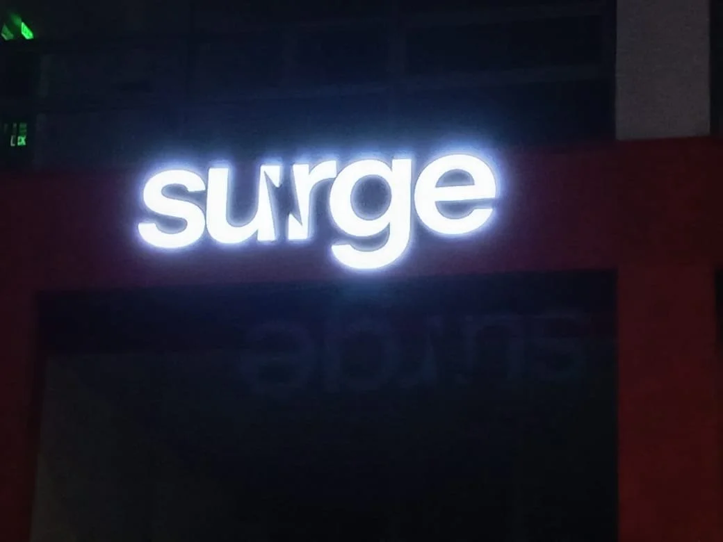 Illuminated white sign with the word 'surge' on a dark background.