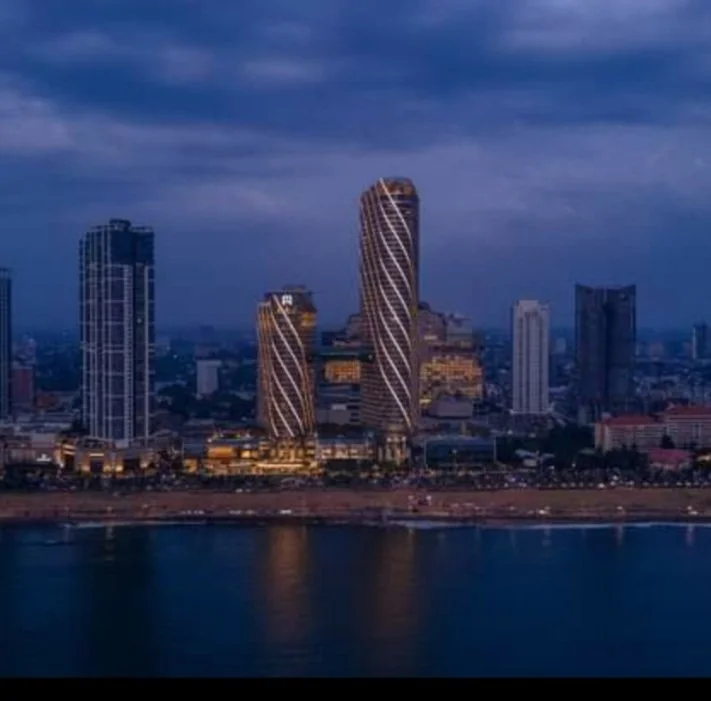City skyline at dusk with high-rise buildings along a waterfront, including two distinctive towers with spiral patterns.