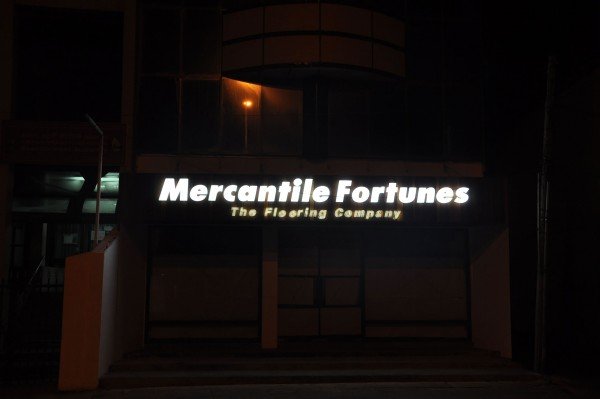 Illuminated sign reading 'Mercantile Fortunes The Flooring Company' outside a building at night.