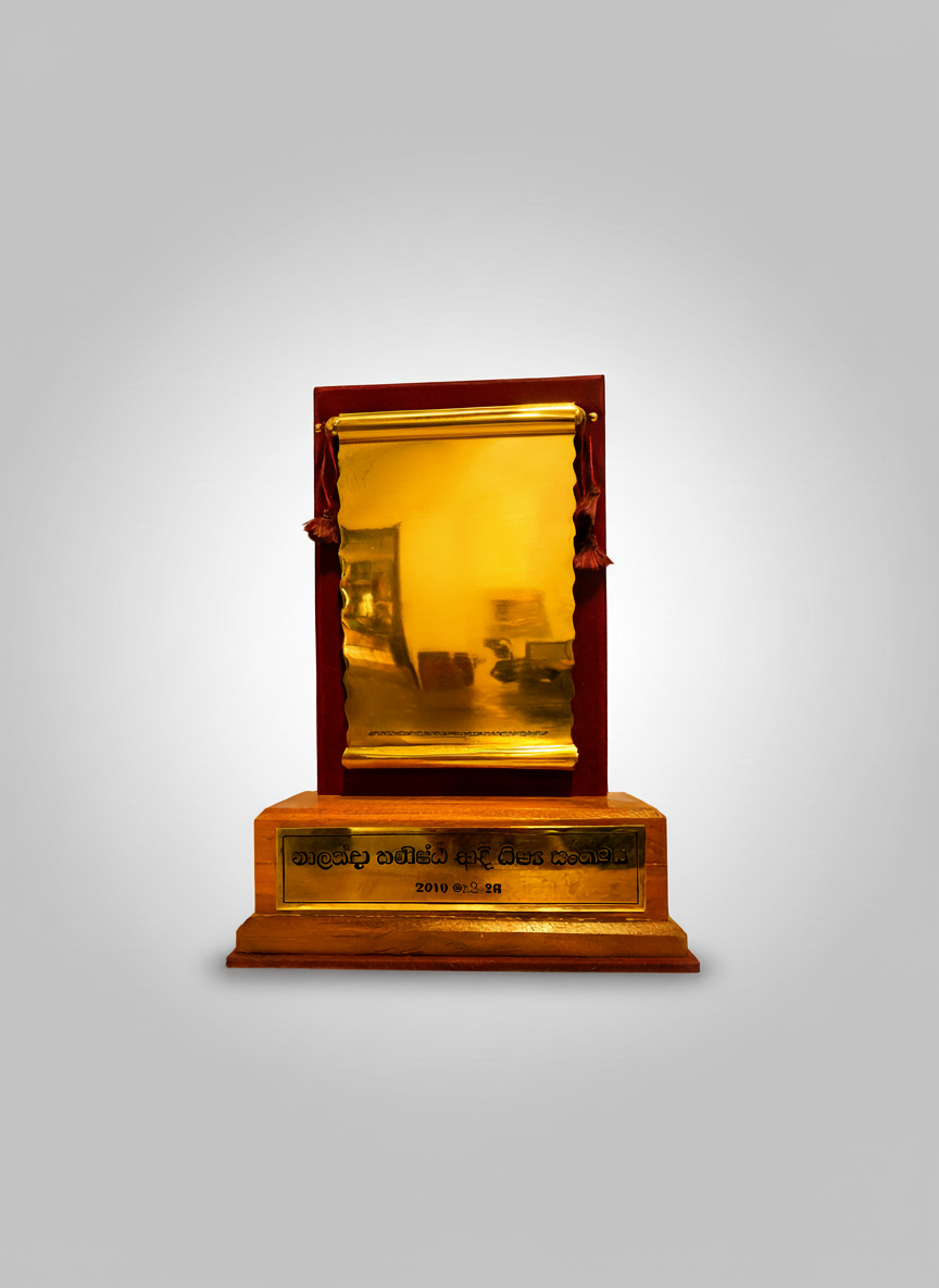 A gold-colored mirror with a wooden stand and red velvet framing, featuring an inscription plate at the base with Sinhala and Tamil writing and a date of 2010.