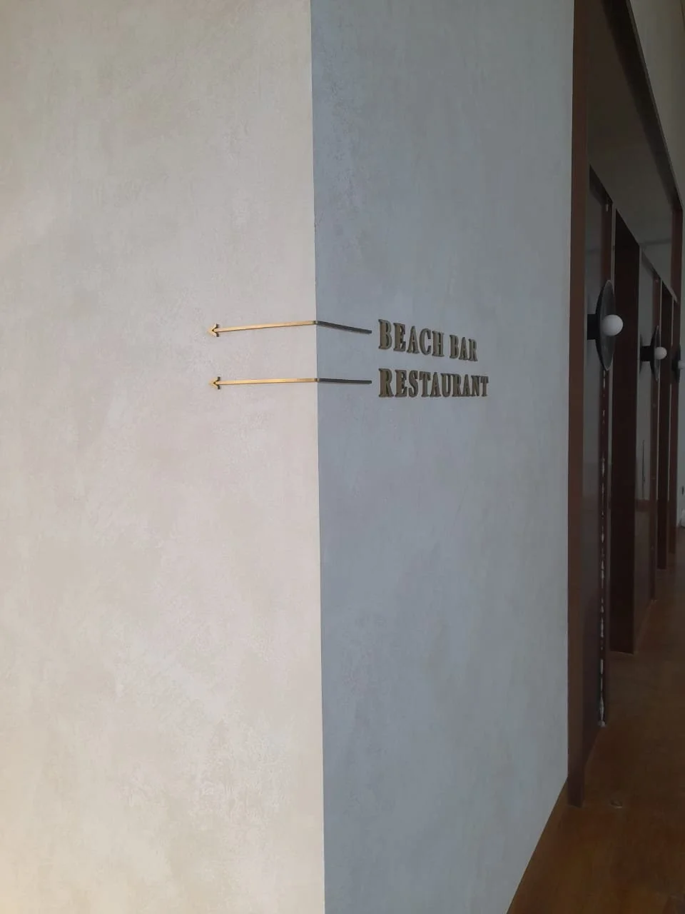 Sign on a wall with two arrows pointing left, indicating directions to a beach bar and a restaurant.