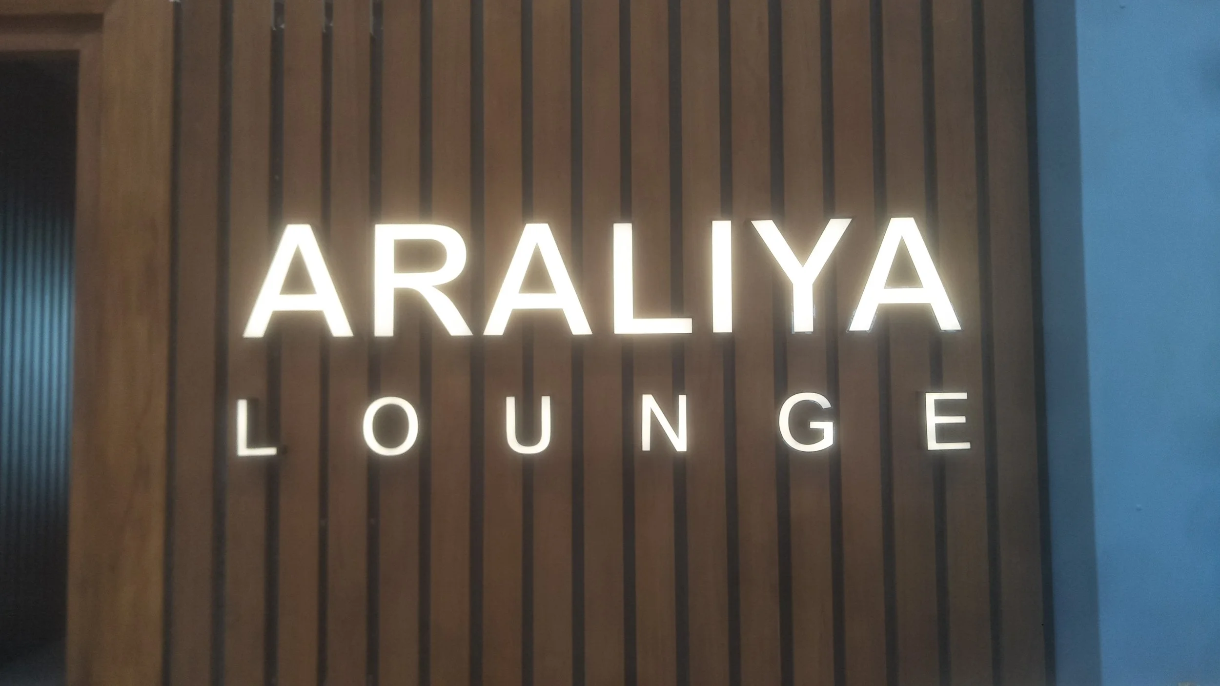 Illuminated sign with the words 'ARALY A LOUNGE' on a wooden slat background.
