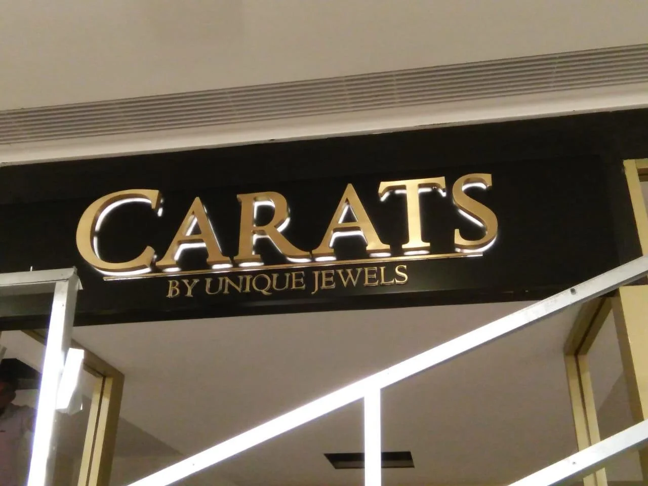 Store sign reading 'CARA TS by Unique Jewels' with illuminated gold letters on black background.