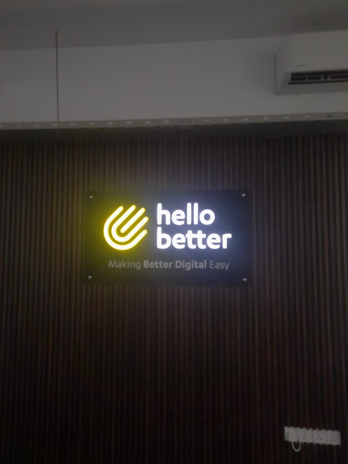 Illuminated sign that reads 'hello better' with a logo and the slogan 'Making Better Digital Easy' on a dark wall.
