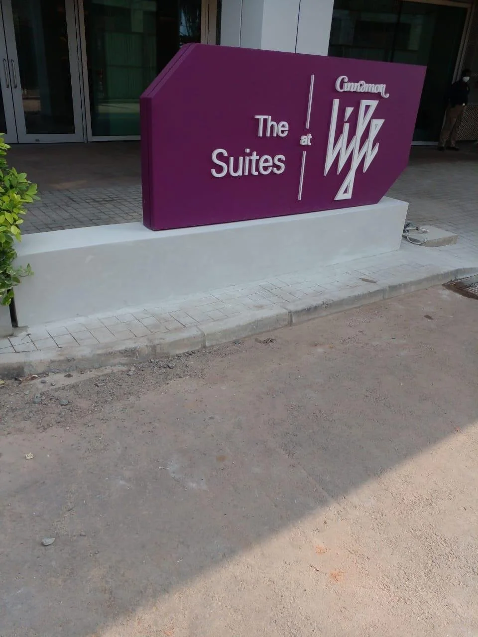 Sign for The Guoman at The Suites hotel with purple background and white text, located outside a building entrance.