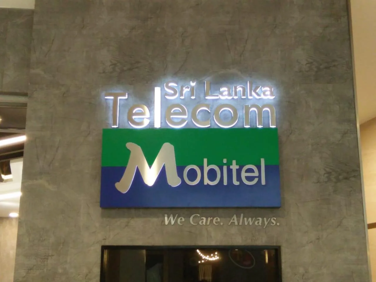 Sign for Sri Lanka Telecom Mobitel with the slogan "We Care. Always." on a stone wall.
