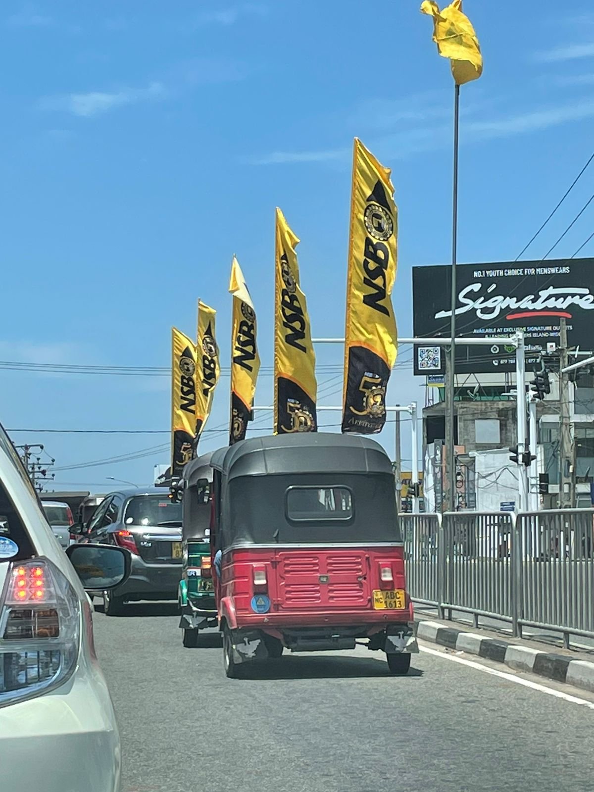Traffic on a busy street with yellow flags and an auto rickshaw in the foreground.