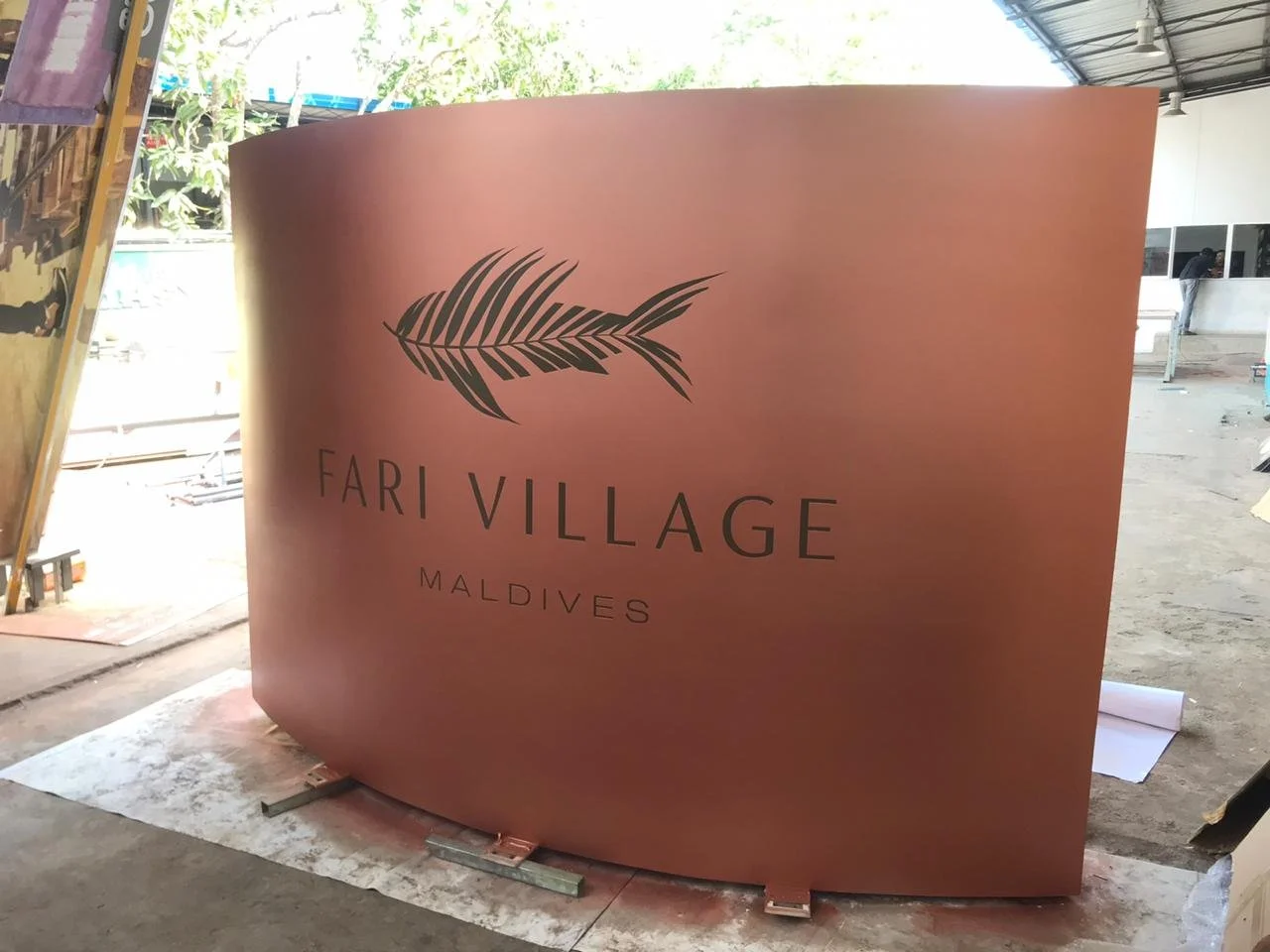 A curved pink sign with a palm leaf graphic and the text "Fari Village Maldives."