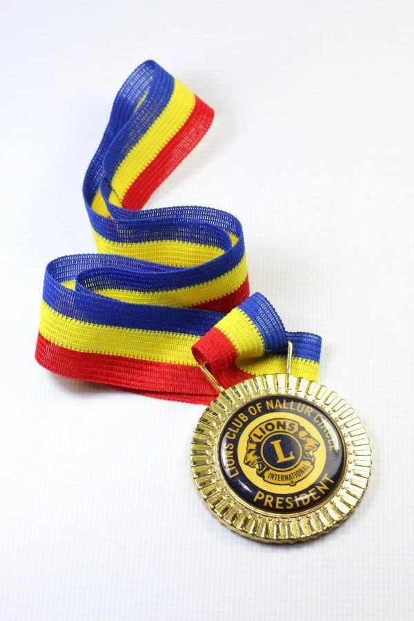 A gold-colored medal with a blue and yellow ribbon. The medal has the Lions Club logo and the words 'Lions Club of Nallur City President'.