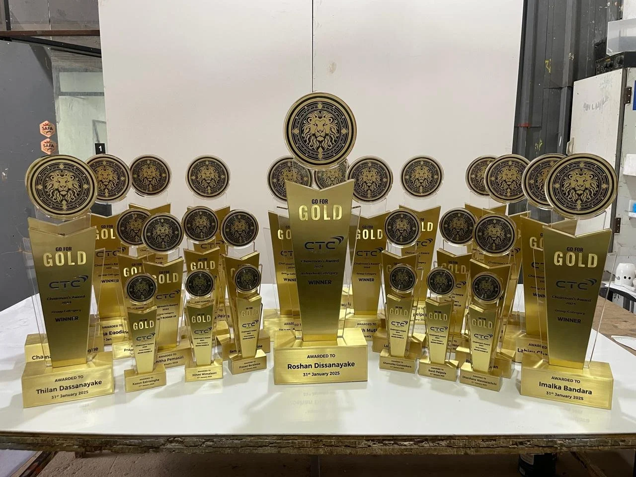 Multiple gold and black trophies with lion emblem, awarded to various individuals, displayed on a table. The trophies are for an award show, dated January 31, 2025, with the central larger trophy labeled 'Go for Gold' and 'Winner' awarded to Roshan D