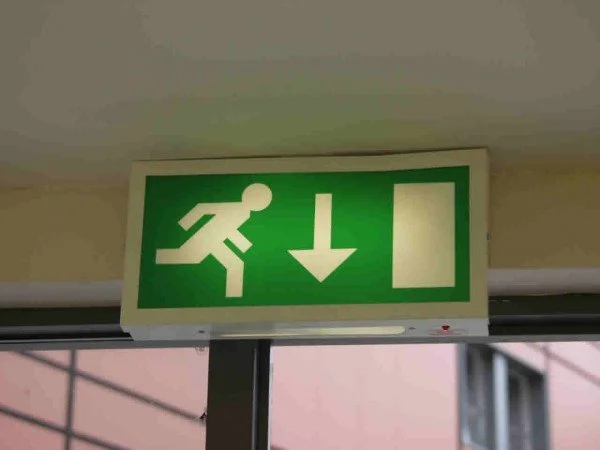 Green emergency exit sign with a running figure, downward arrow, and a box.