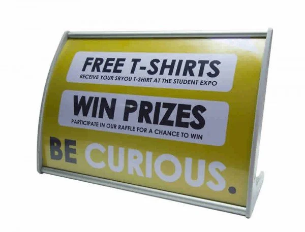 Yellow promotional sign offering free T-shirts at the student expo, with a chance to win prizes through a raffle, and encouraging viewers to be curious.