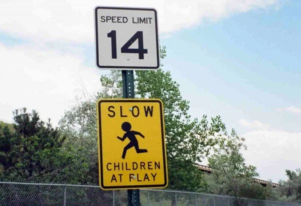 A road sign showing a speed limit of 14 miles per hour and a yellow warning sign indicating slow children at play.