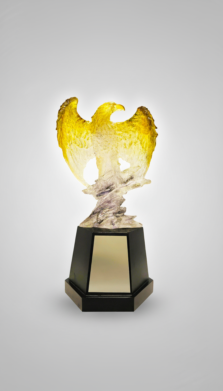 Glass sculpture of a golden eagle with outstretched wings on a black stand.