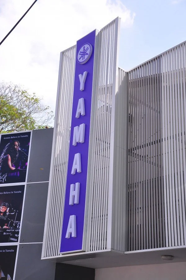 Vertical blue sign with white letters spelling 'YAMAHA' on a modern building facade.