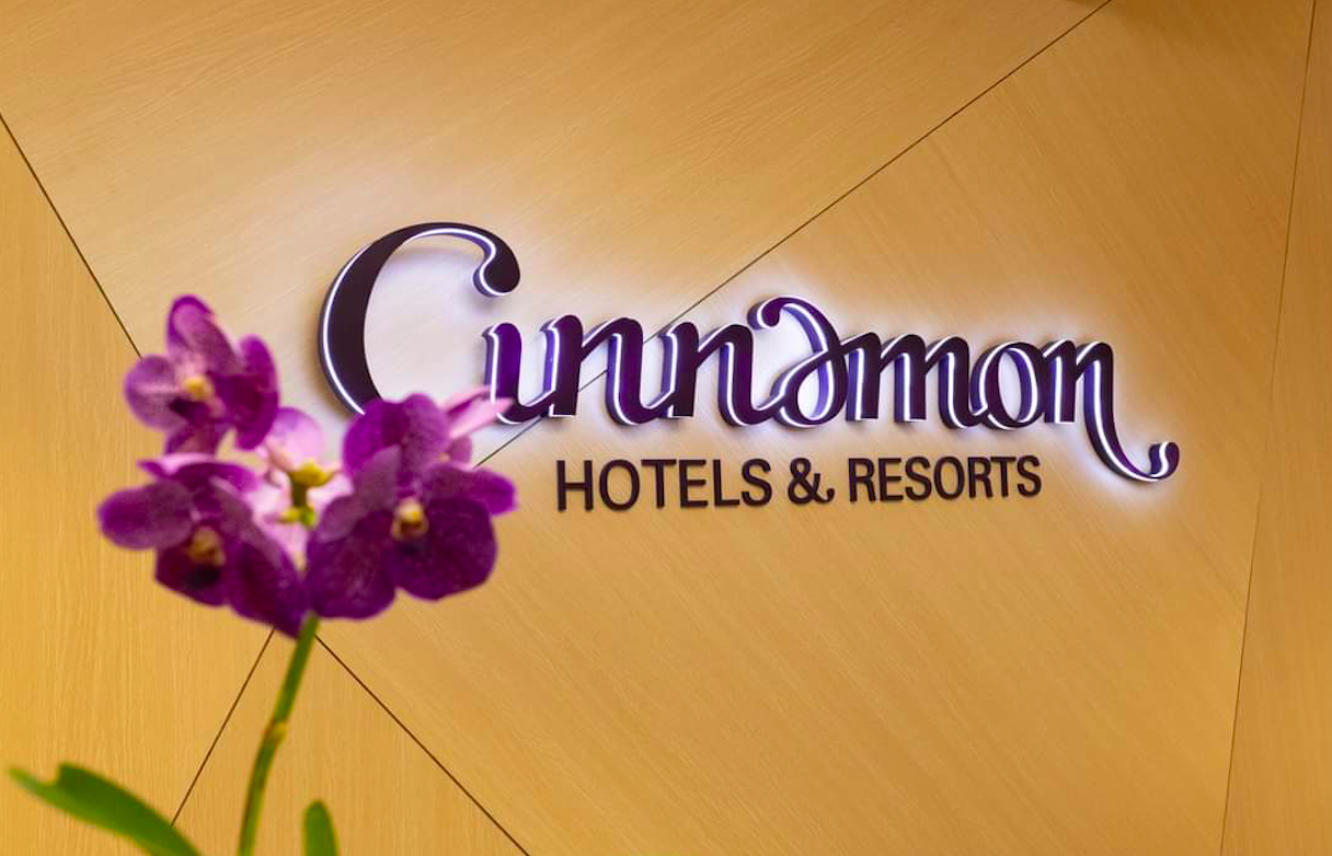 Sign for Gunumon Hotels & Resorts on a wooden wall with a purple orchid flower in the foreground.