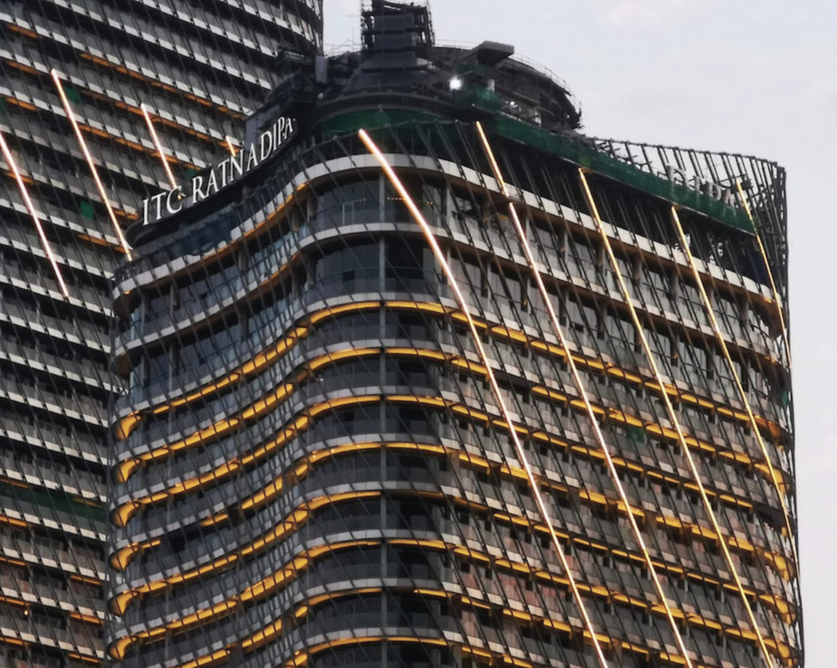 Close-up of a high-rise building with curved architecture, illuminated by horizontal orange and yellow lights, and a sign in the upper part that reads 'ITC RATTANADIPU'.