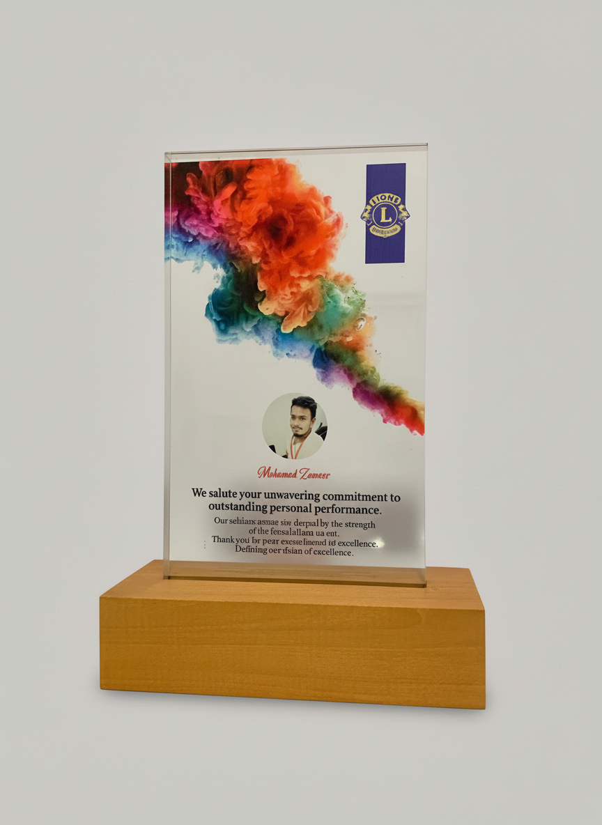 A glass award with a colorful smoke design, mounted on a wooden base, featuring a photo and a message of recognition for Mohamed Zameer.