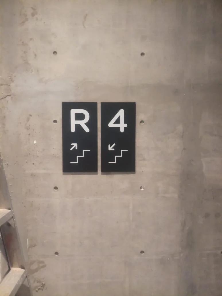 Sign on a concrete wall showing directions to R4 and a staircase, with arrows pointing upstairs for R and downstairs for 4.