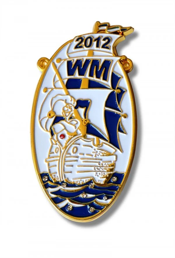 A decorative gold and blue enamel pin featuring a ship, a captain, and the acronym WM, with the year 2012, in an elongated oval shape.