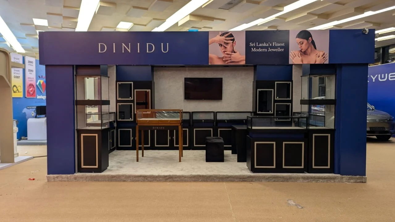 Empty jewelry kiosk with display cases and a large sign that reads 'DINIDU' and 'Sri Lanka's Finest Modern Jeweller' in an indoor mall.