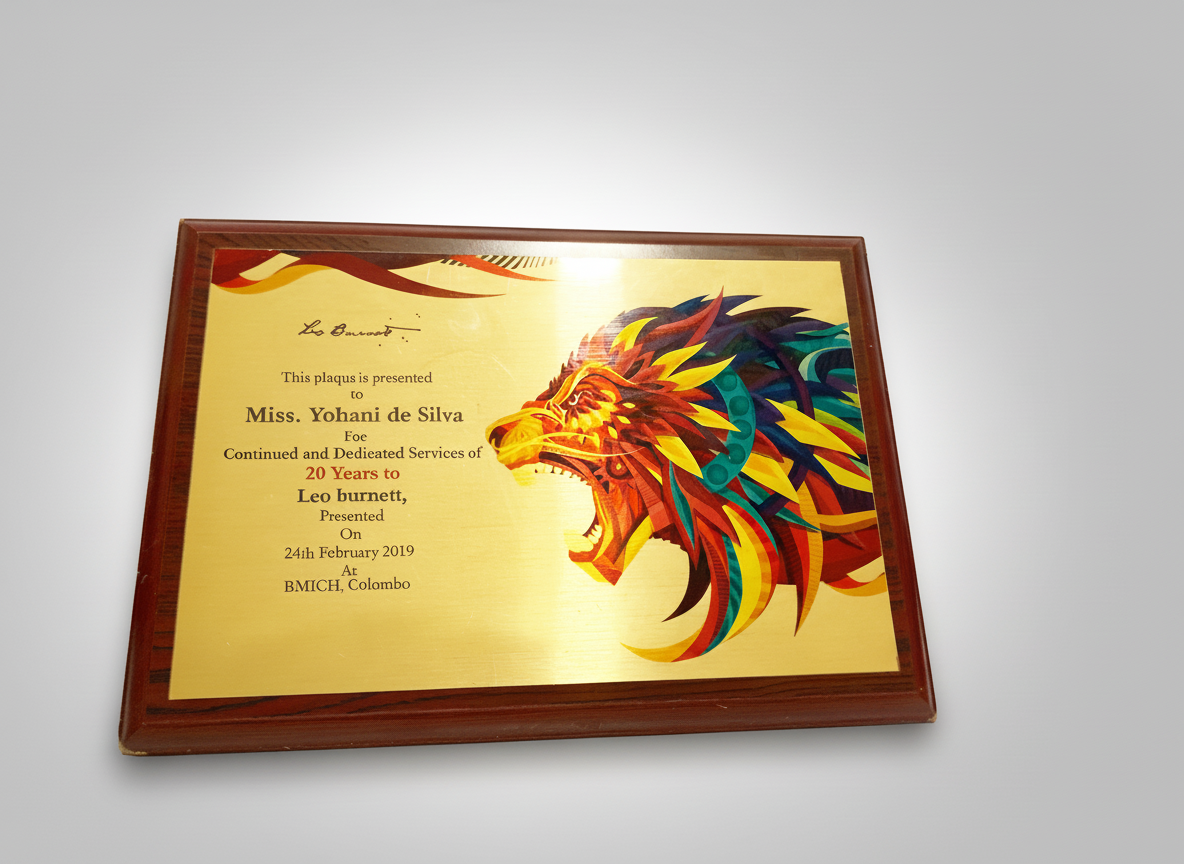 Plaque with a colorful lion illustration and text recognizing Miss. Yohani de Silva's 20 years of service for Leo Burnett, presented at BMICH Colombo in February 2019.