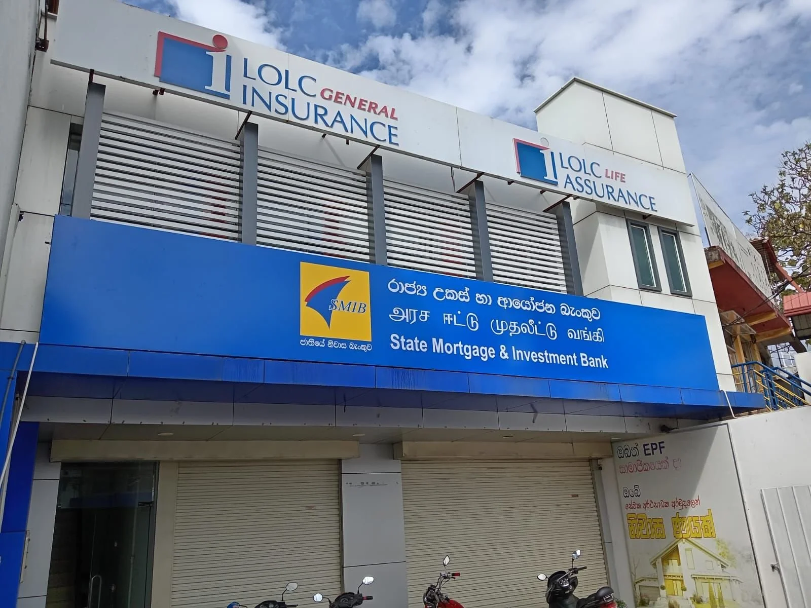Building with multiple signs, including LOLC General Insurance, LOLC Life Assurance, and State Mortgage & Investment Bank, with motorcycles parked in front.