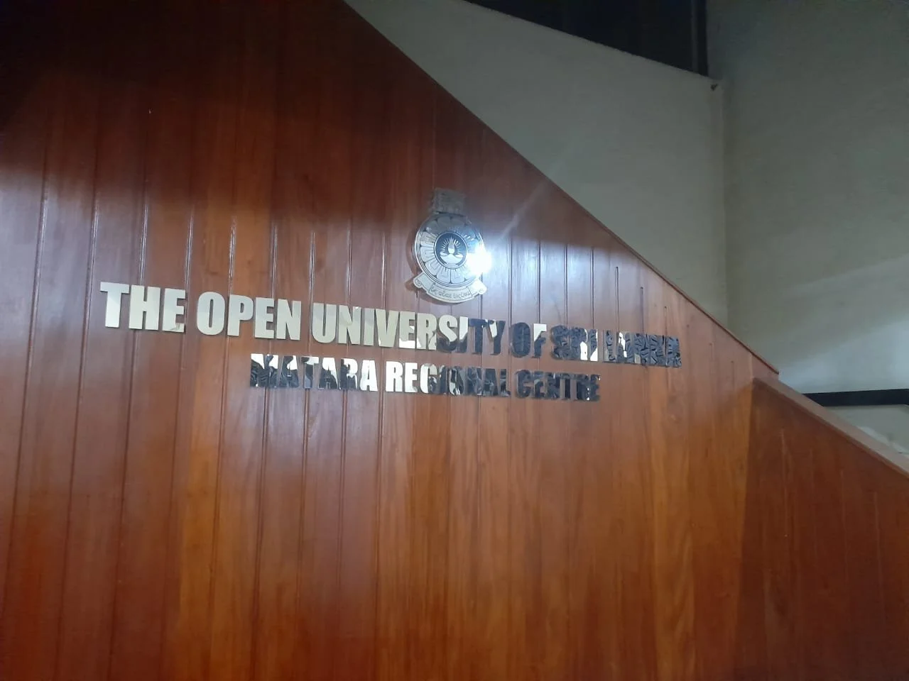 Sign on wooden wall displaying 'The Open University of Sri Lanka, Nuwara Eliya Regional Centre' with a logo above.