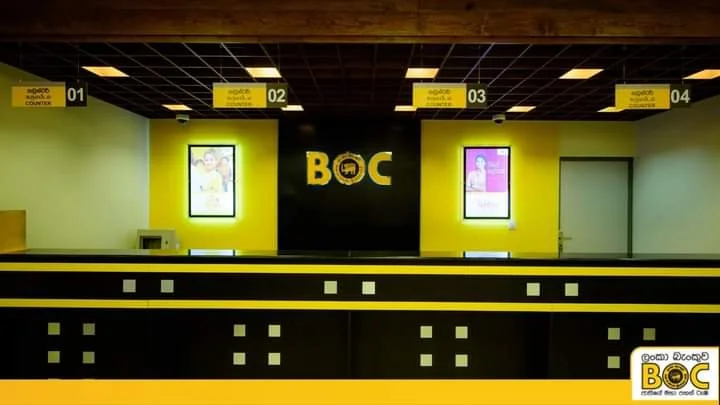 Airport baggage check-in counter with four counters numbered 01 to 04, illuminated yellow signs, bright yellow and black color scheme, two illuminated posters on the wall, and a logo for BOC in the center.