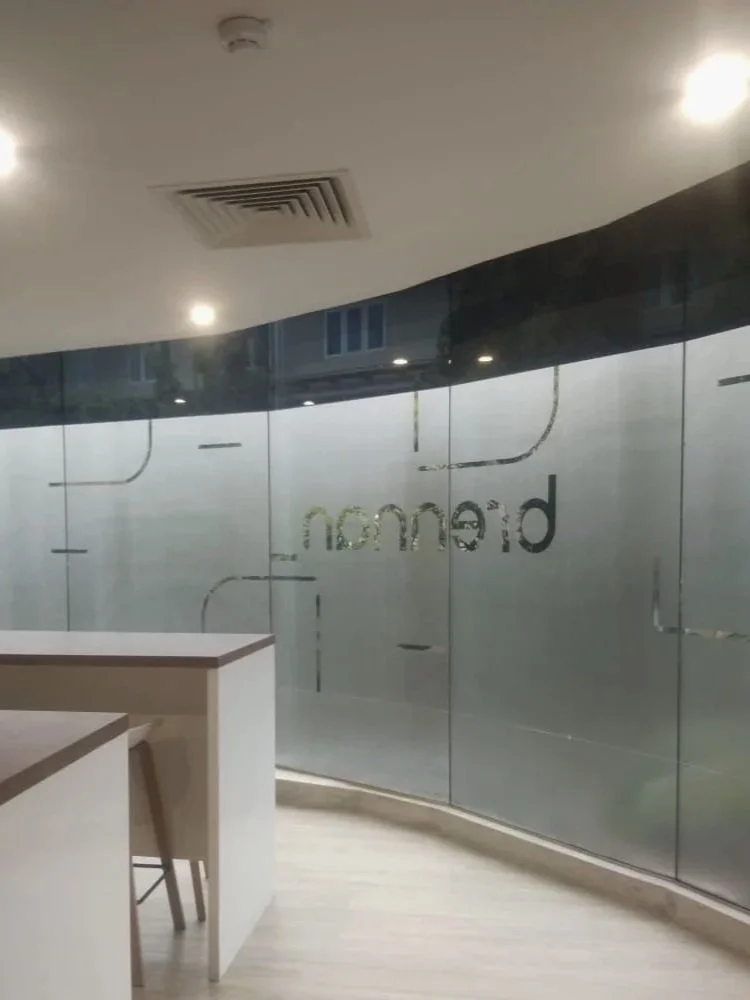 Empty modern office space with glass walls and the word "render" visible, with a corner of a white desk and a chair.