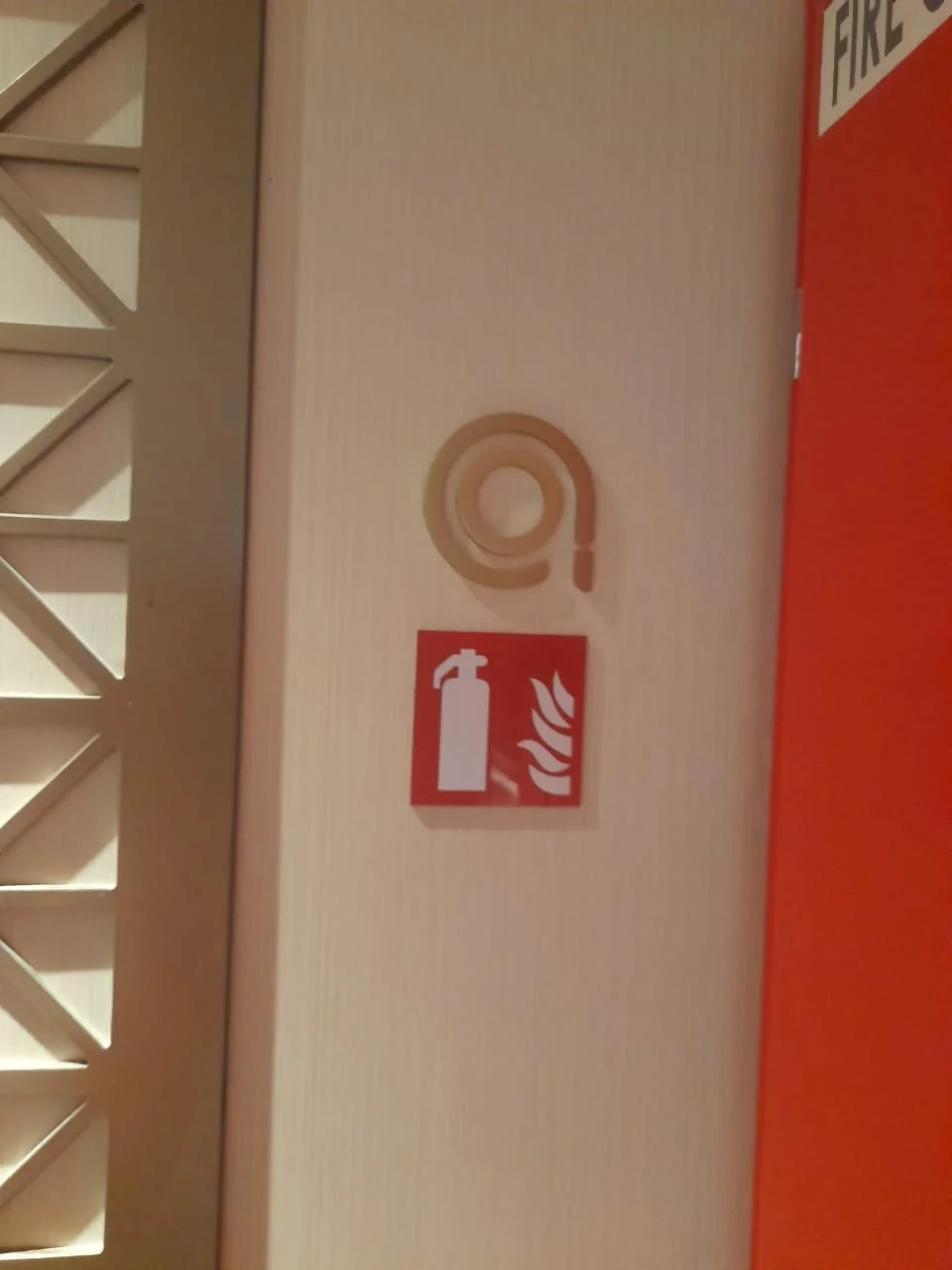 Fire safety equipment sign with a fire extinguisher and flames, and a cable reel on a light-colored wall.