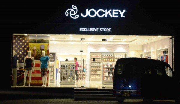 Storefront of Jockey exclusive store at night with mannequins and display shelves visible through the glass window.