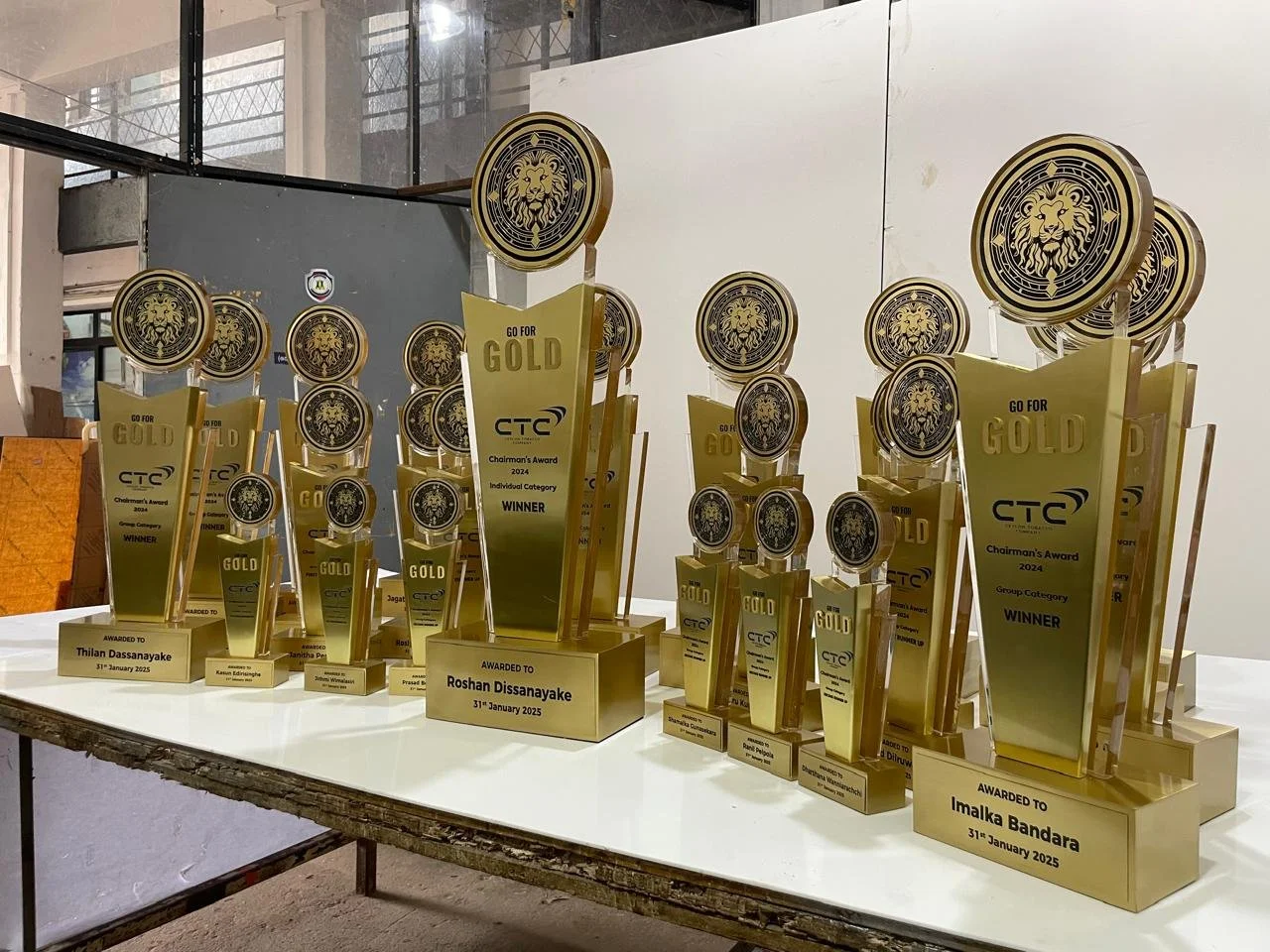 A collection of gold awards trophies with lion logos, lined up on a table, each engraved with recipient's names and awards, for the CTC Chairman's Award 2024, dated January 31, 2025.