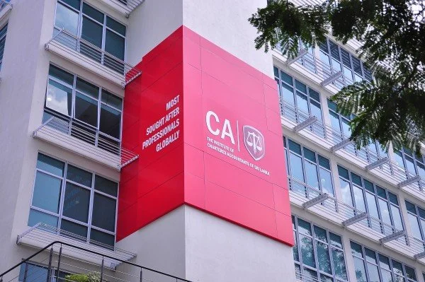 Close-up of a building with a large red sign displaying the CA (Child Advocates) logo and slogan. The sign reads "Most Sought After Professionals Worldwide". The building has multiple windows and balconies, with green trees partially visible.
