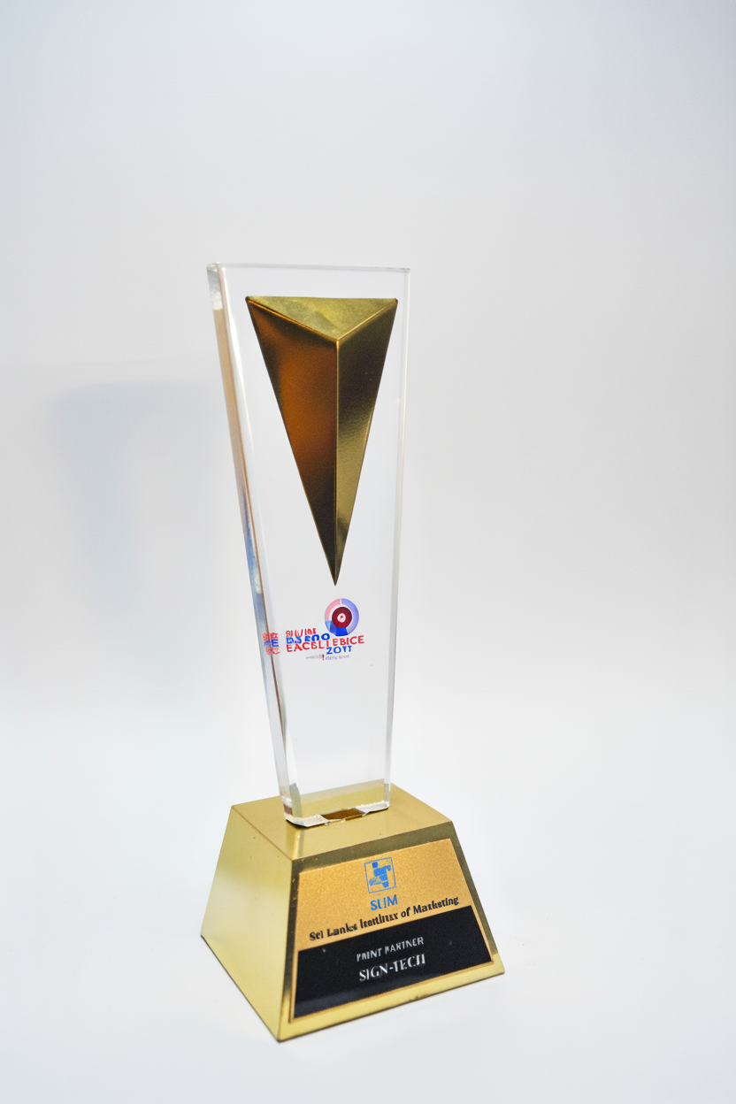 A tall, transparent, rectangular award with a gold and black geometric design at the top, mounted on a gold base with a black plaque. The plaque reads 'SLUM, Srl Lanka Institute of Marketing, PRINT PARTNER, SIGN-TECU'.