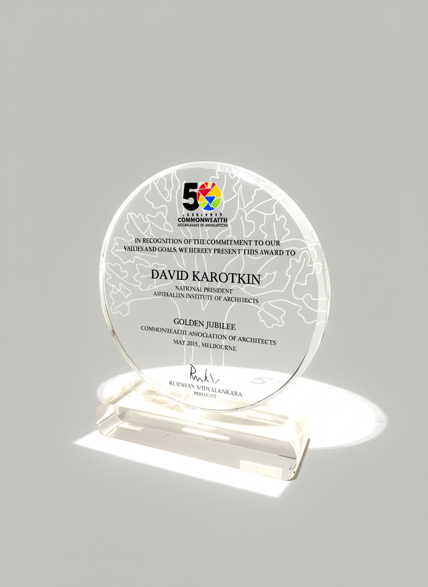 A clear acrylic award plaque with engraved text and a colorful logo at the top, mounted on a white base, celebrating a Golden Jubilee for the Commonwealth Architects Association in May 2015 at Melbourne.