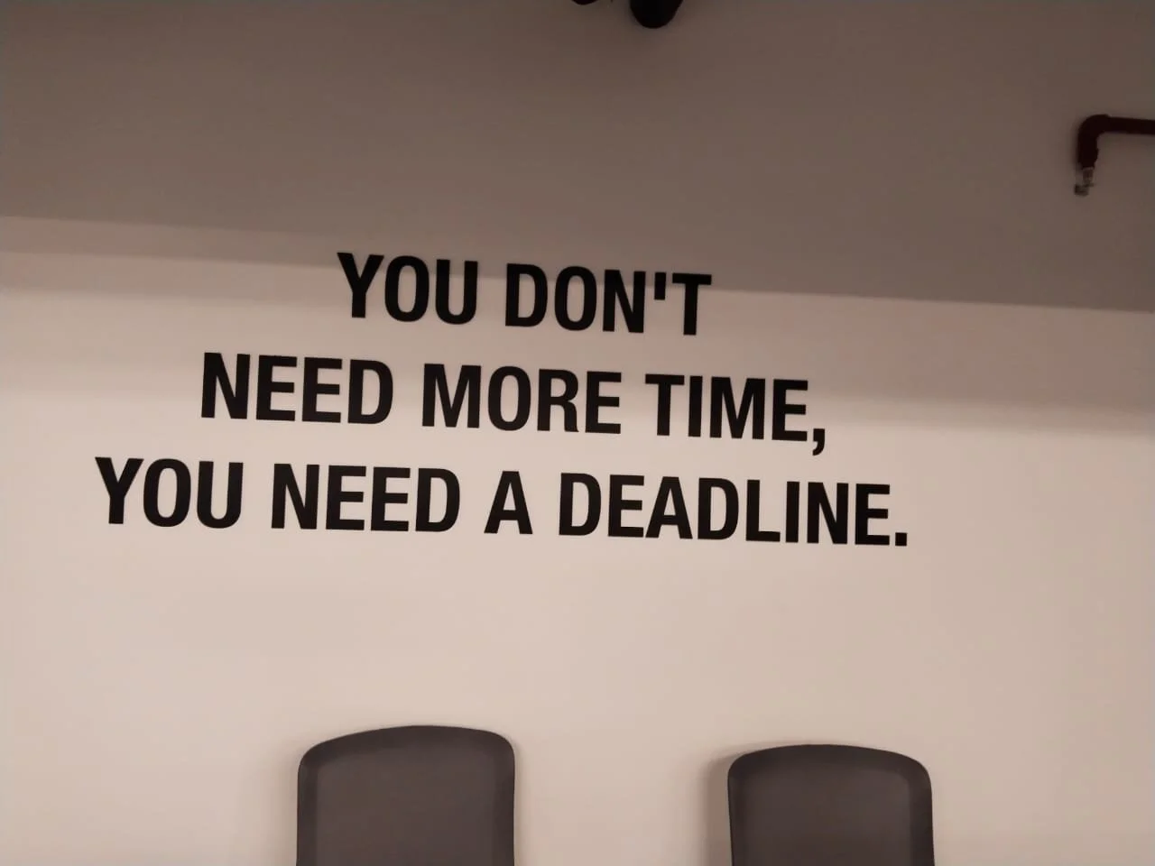 A motivational quote on a wall that says, 'You don't need more time, you need a deadline,' with two sofas in front.