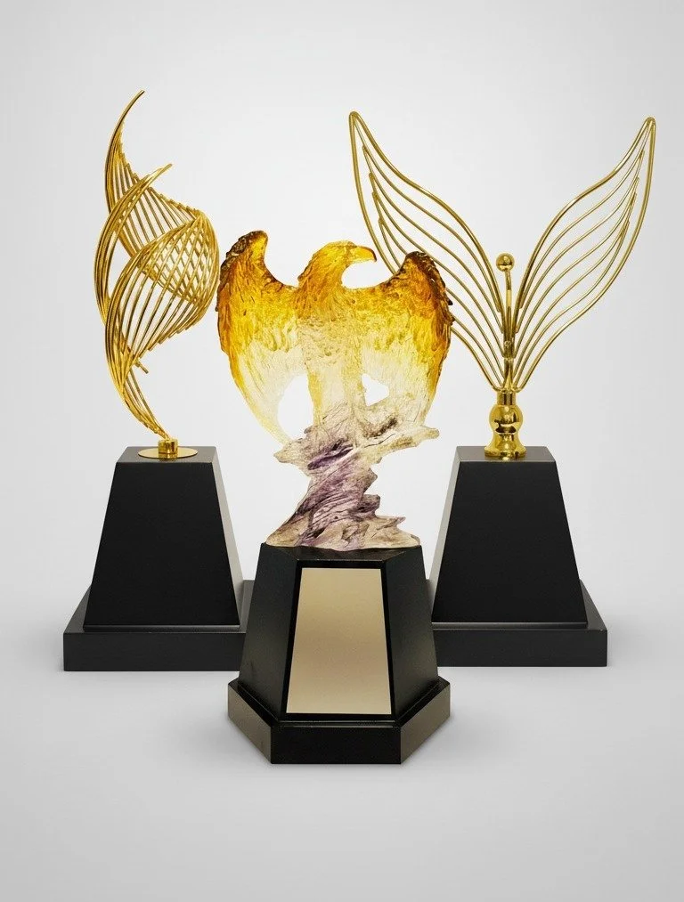 Three trophy awards with a gold eagle figure in the center and wing-like structures on either side, all mounted on black bases.