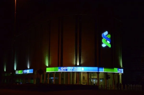A large, dark stadium or arena with illuminated signage and a glowing logo on the exterior at night.