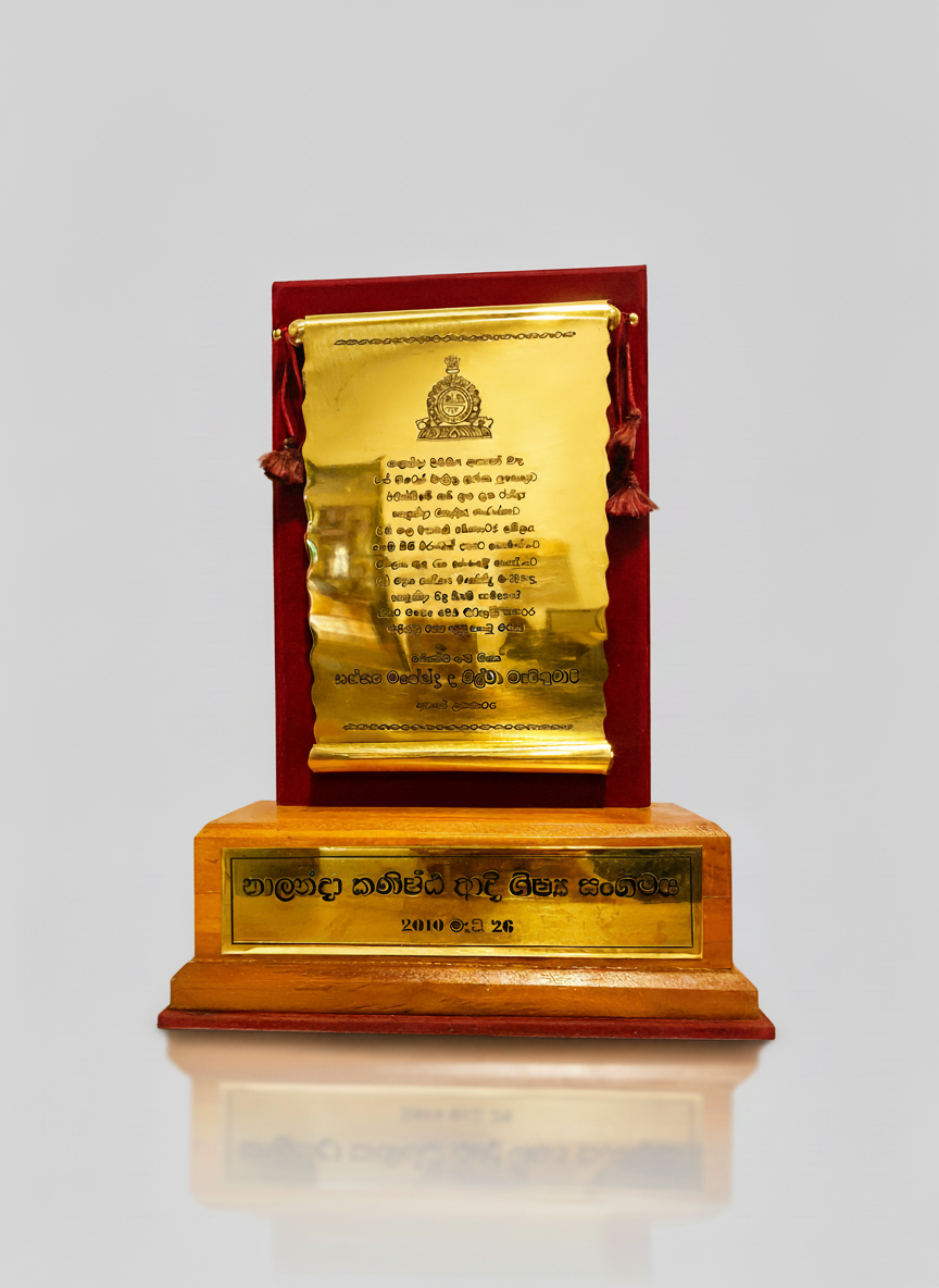 A golden plaque mounted on a wooden base with Sri Lankan script and a date, 2010 02 26, engraved on it.