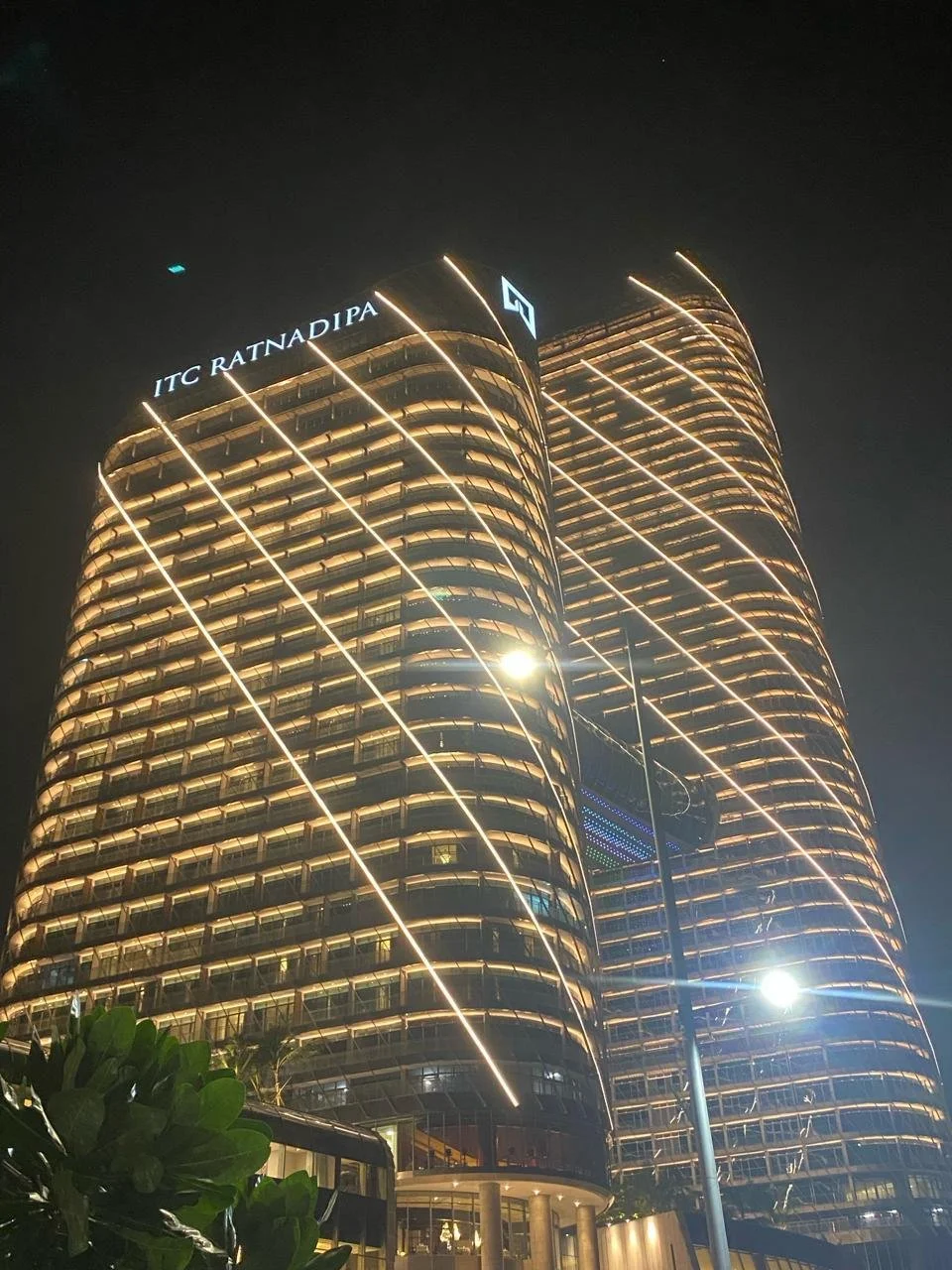Night view of two tall, modern office buildings with glass facades illuminated by lights. The buildings are labeled 'ITC RATNA DIPA' at the top.