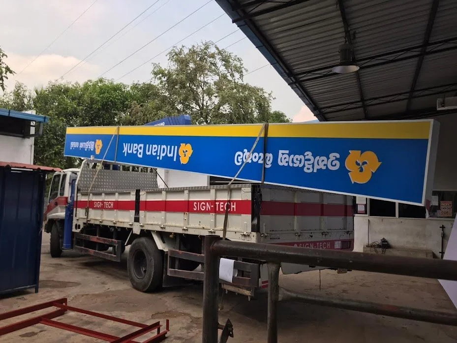 A truck parked at a workshop with a large sign for Iland Bank resting on top of it, tilted to one side.