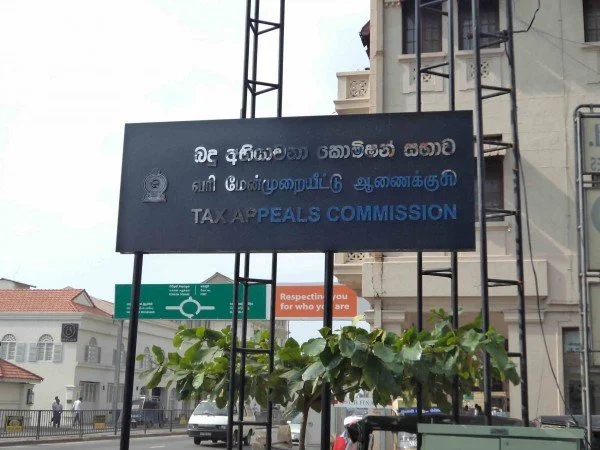 Street scene with a sign for the Tax Appeals Commission in front of a building and plants.