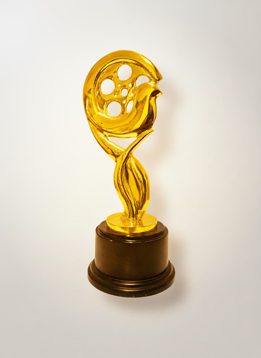 Golden trophy sculpture resembling a film reel with a stylized film strip, mounted on a round black base.