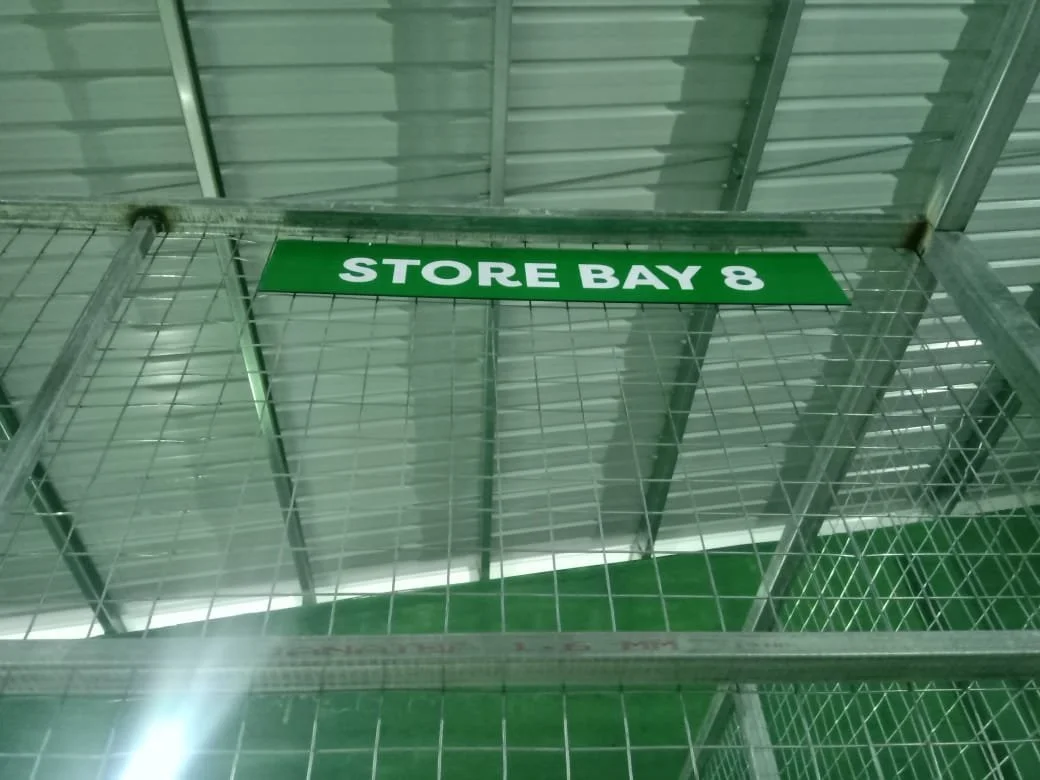 A metal shopping cart with a green sign that reads 'STORE BAY 8' attached to it inside a store with a metal ceiling.