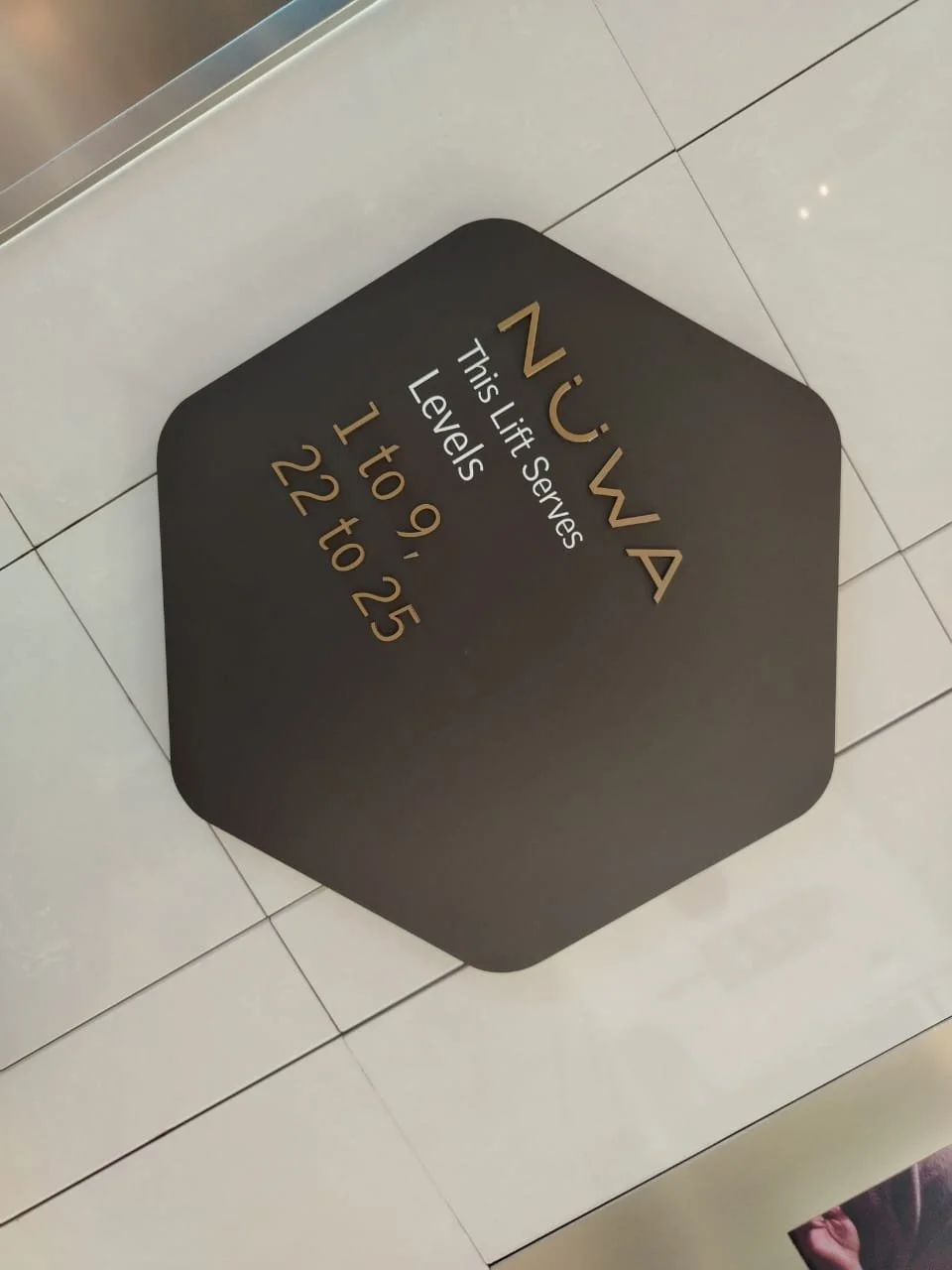 Black hexagonal floor sign with gold and white lettering indicating elevator levels N, W, and A, with specific levels listed as 1 through 25.