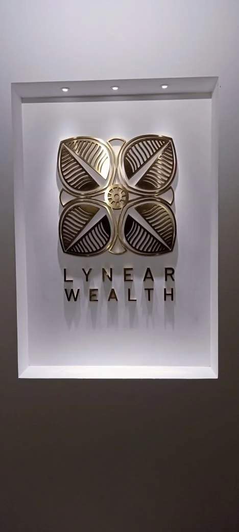 Decorative wall sign featuring four golden leaves and the text 'LYNEAR WEALTH' in gold letters.