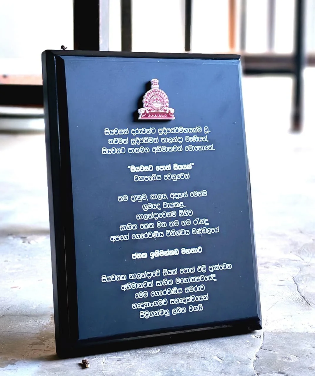 A black signboard with a university emblem at the top and text in Sinhala language.