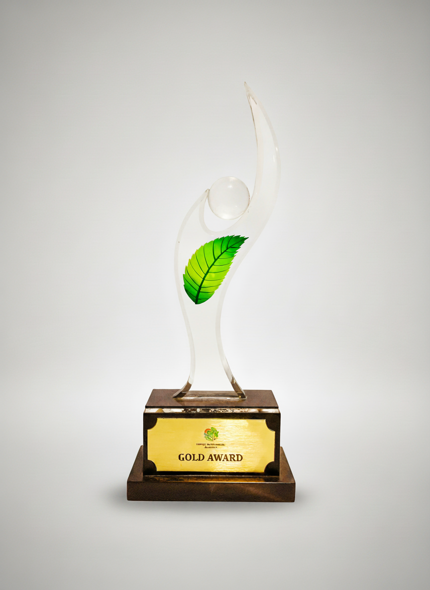 A glass award trophy with a green leaf decoration and a round glass element on top, mounted on a wooden base with a gold plaque that says 'GOLD AWARD' and a small logo above it.