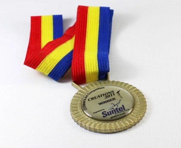 Medal with a striped ribbon in red, yellow, and blue, awarded at the 2011 Championship All Competition, sponsored by Suntel, with an inscription indicating the winner.